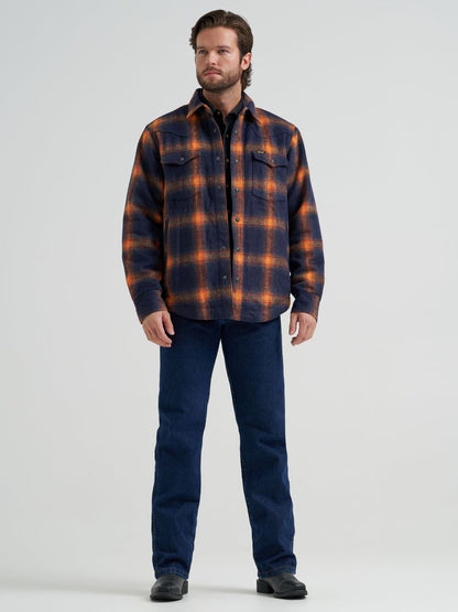 Man wearing a blue and orange Wrangler flannel jacket and blue jeans on a grey background