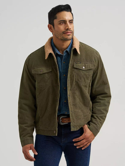 A man wearing an olive green Wrangler corduroy jacket with a tan sherpa collar, layered over a blue denim shirt and jeans, photographed against a light gray studio background.