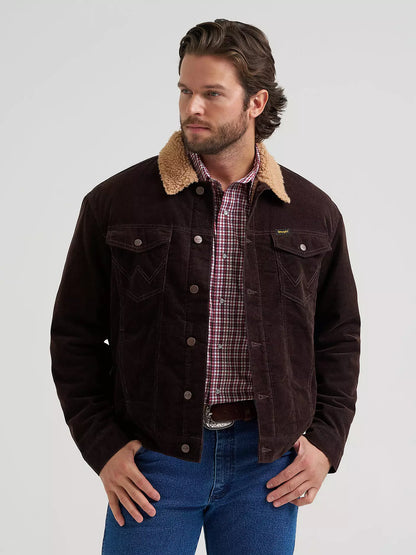 A man wearing a dark brown corduroy Wrangler jacket with a tan sherpa collar, layered over a red and white plaid button-down shirt and blue jeans, photographed against a light gray studio background.