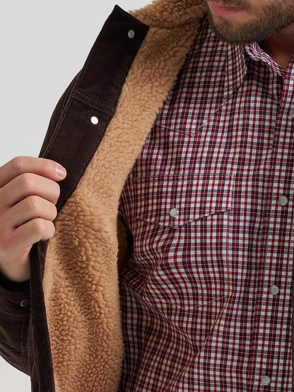 Close-up of a person wearing a brown Wrangler corduroy jacket with a tan sherpa lining over a red and white plaid button-down shirt.