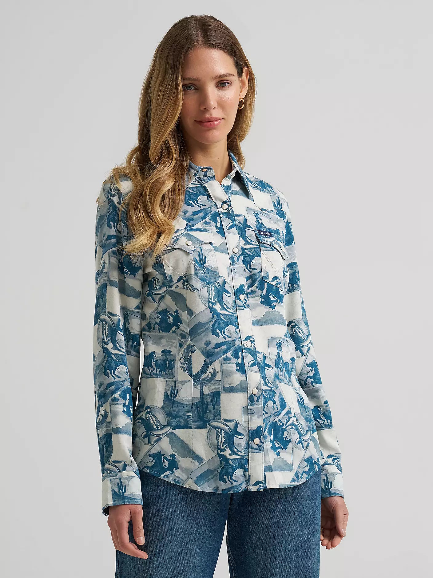 A woman wearing a long-sleeve button-up shirt from Wrangler with a blue and white collage print, paired with blue jeans, shown against a light gray studio background.