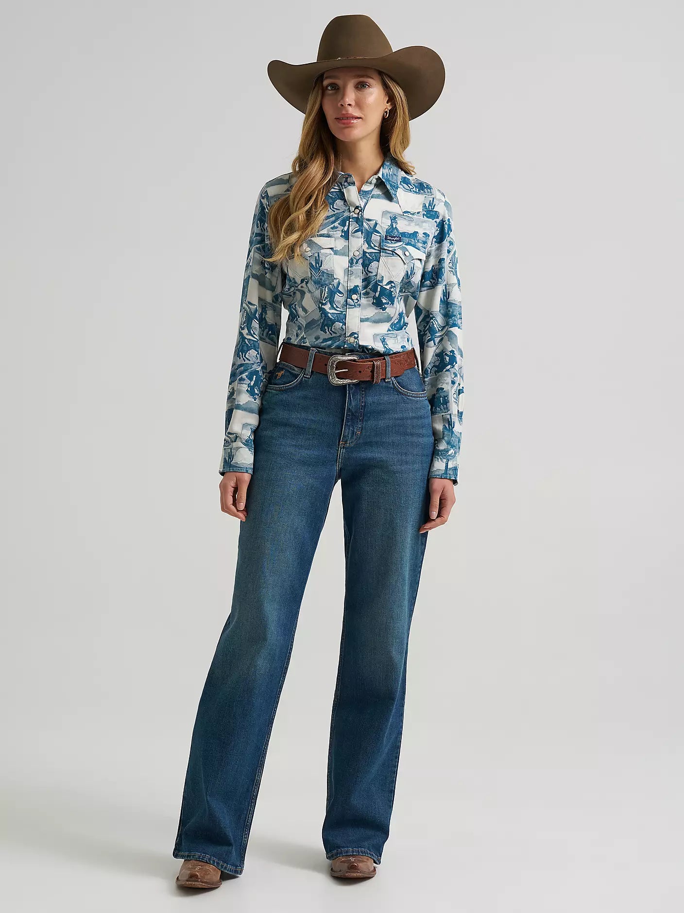 A woman wearing a long-sleeve button-up shirt from Wrangler with a blue and white collage print, paired with blue jeans, shown against a light gray studio background.