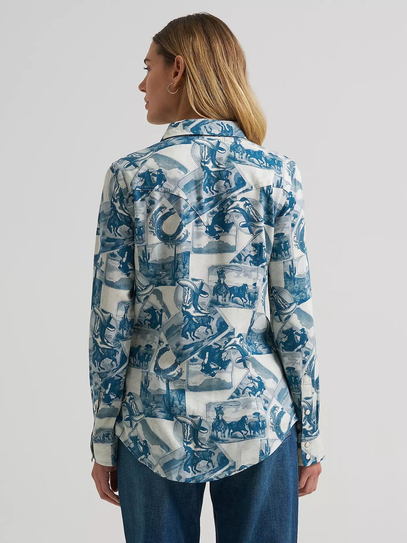 A woman wearing a long-sleeve button-up shirt from Wrangler with a blue and white collage print, paired with blue jeans, shown against a light gray studio background.