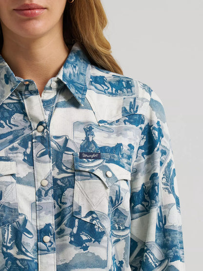 A close-up of a woman wearing a blue and white printed button-up shirt from Wrangler with a visible Wrangler logo patch on the chest pocket.
