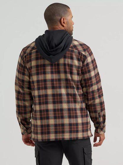 A man wearing a hooded plaid Wrangler jacket with a brown, beige, and black pattern, paired with black cargo pants, photographed against a light gray studio background.