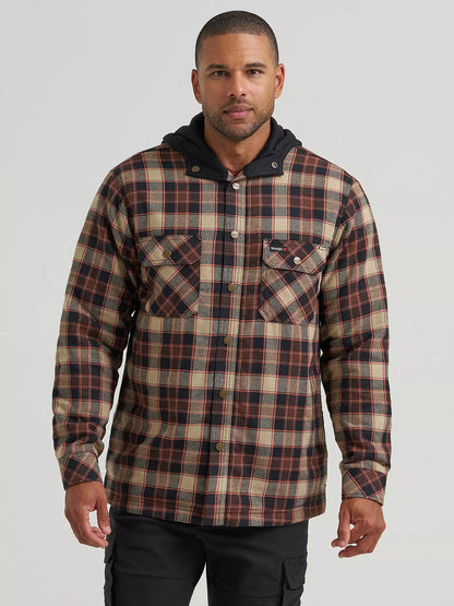 A man wearing a hooded plaid Wrangler jacket with a brown, beige, and black pattern, paired with black cargo pants, photographed against a light gray studio background.