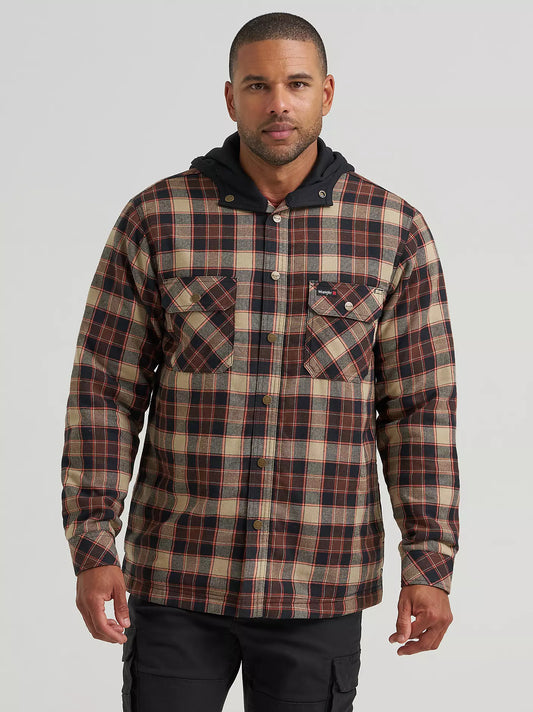 A man wearing a hooded plaid Wrangler jacket with a brown, beige, and black pattern, paired with black cargo pants, photographed against a light gray studio background.