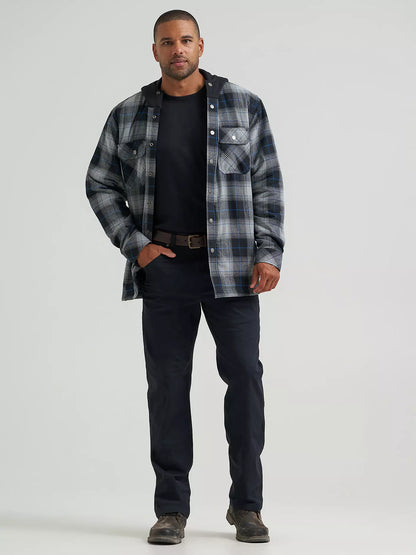 A man wearing a long-sleeve plaid hooded Wrangler Jacket in gray, black, and blue, paired with a black t-shirt and dark pants, against a solid light gray background.