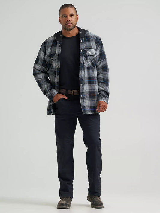 A man wearing a long-sleeve plaid hooded Wrangler Jacket in gray, black, and blue, paired with a black t-shirt and dark pants, against a solid light gray background.