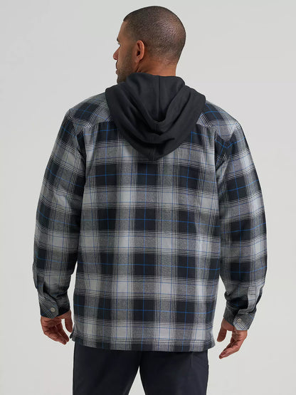 A man wearing a long-sleeve plaid hooded Wrangler Jacket in gray, black, and blue, paired with a black t-shirt and dark pants, against a solid light gray background.