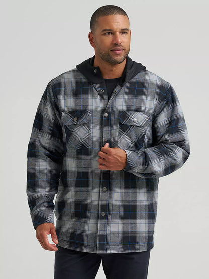 A man wearing a long-sleeve plaid hooded Wrangler Jacket in gray, black, and blue, paired with a black t-shirt and dark pants, against a solid light gray background.