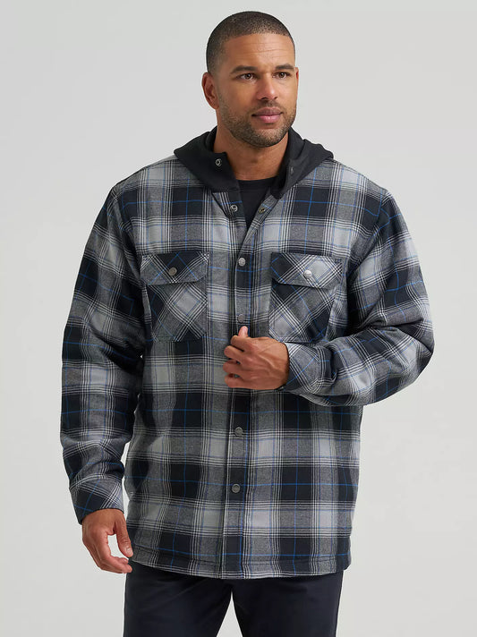 A man wearing a long-sleeve plaid hooded Wrangler Jacket in gray, black, and blue, paired with a black t-shirt and dark pants, against a solid light gray background.