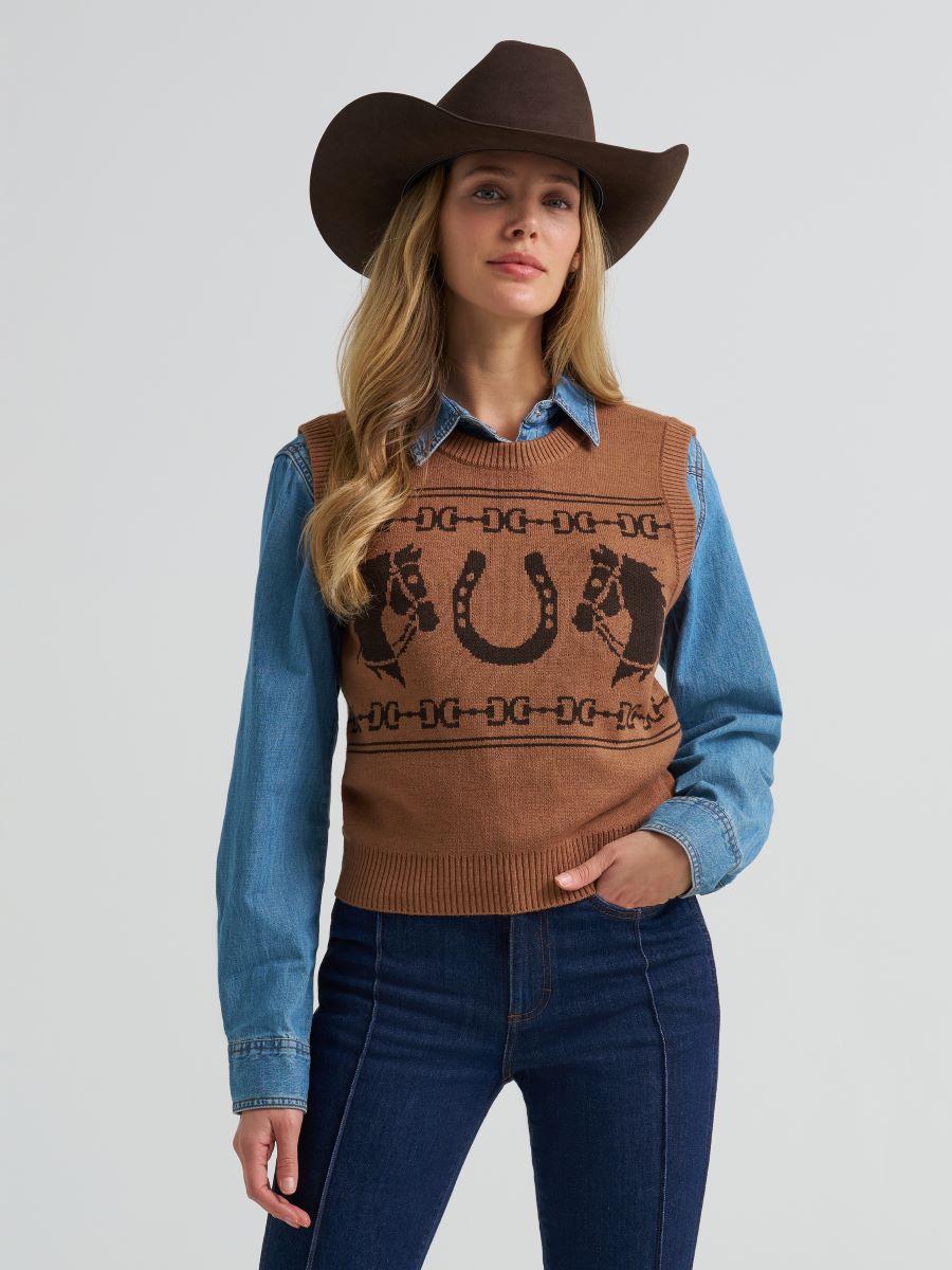Woman wearing a brown Wrangler horse patterned vest over a blue shirt with a cowboy hat on a gray background