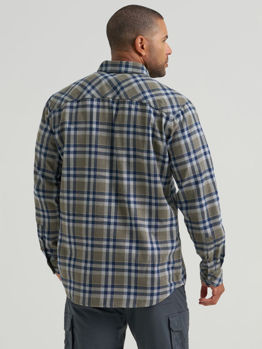 A man wearing a Wrangler long-sleeve plaid button-up shirt in a muted green, blue, and white pattern, shown from a rear three-quarter view against a light gray studio background.