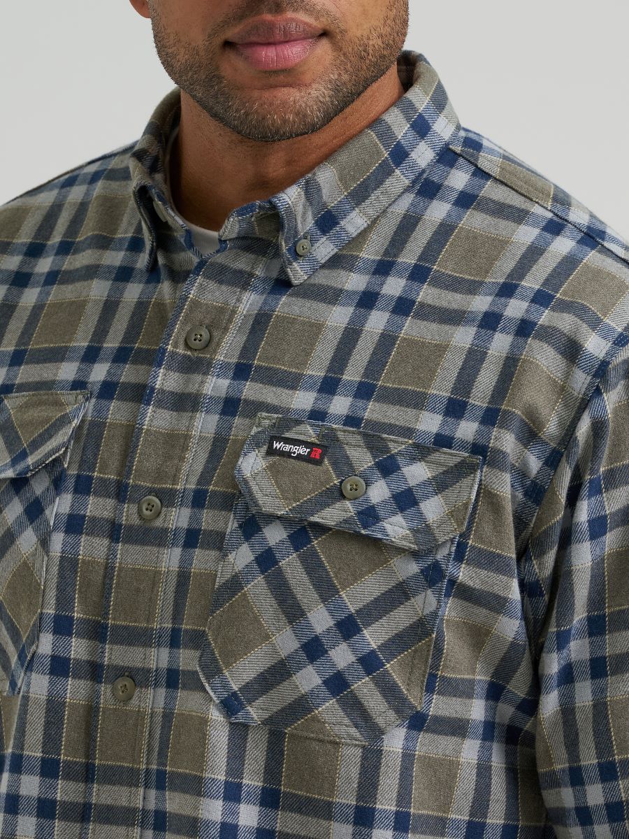 Close-up of a man wearing a Wrangler plaid button-down shirt in blue, gray, and olive tones, showing the chest pocket with a visible Wrangler logo tab.