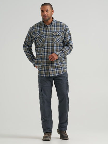 A man modeling a long-sleeve Wrangler plaid button-up shirt in blue, gray, and white, paired with dark gray cargo pants and brown shoes, against a light gray studio background.