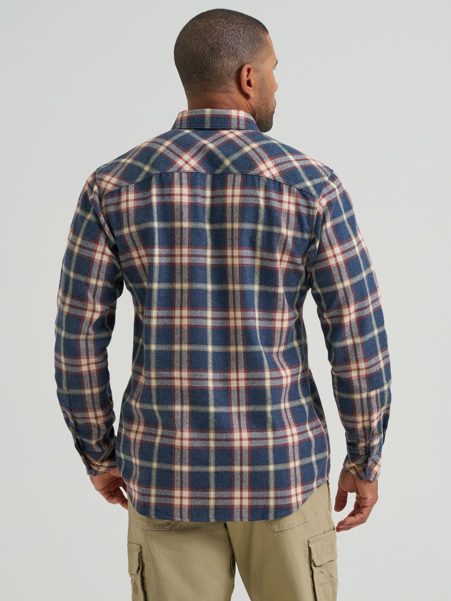 A man viewed from the back wearing a long-sleeve plaid button-up Wrangler shirt in navy blue, beige, and red, paired with khaki cargo pants, against a light gray studio background.