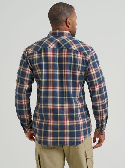 A man viewed from the back wearing a long-sleeve plaid button-up Wrangler shirt in navy blue, beige, and red, paired with khaki cargo pants, against a light gray studio background.