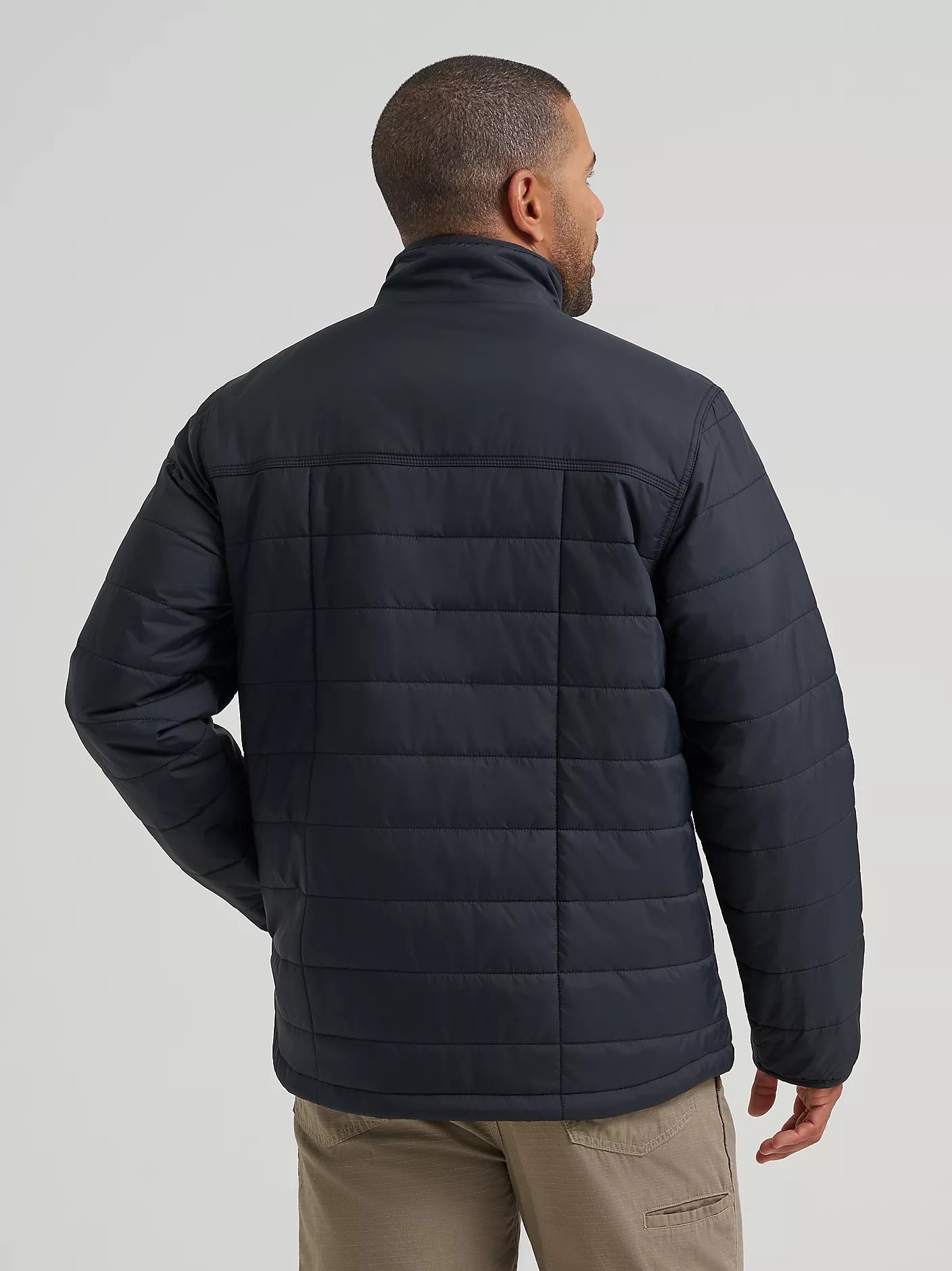A man wearing a black Wrangler quilted puffer jacket, shown from the back against a light gray studio background.