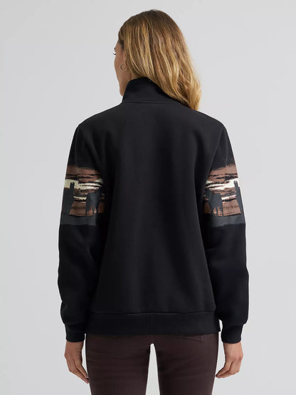 Woman wearing a black Wrangler pullover with patterned sleeves on a gray background