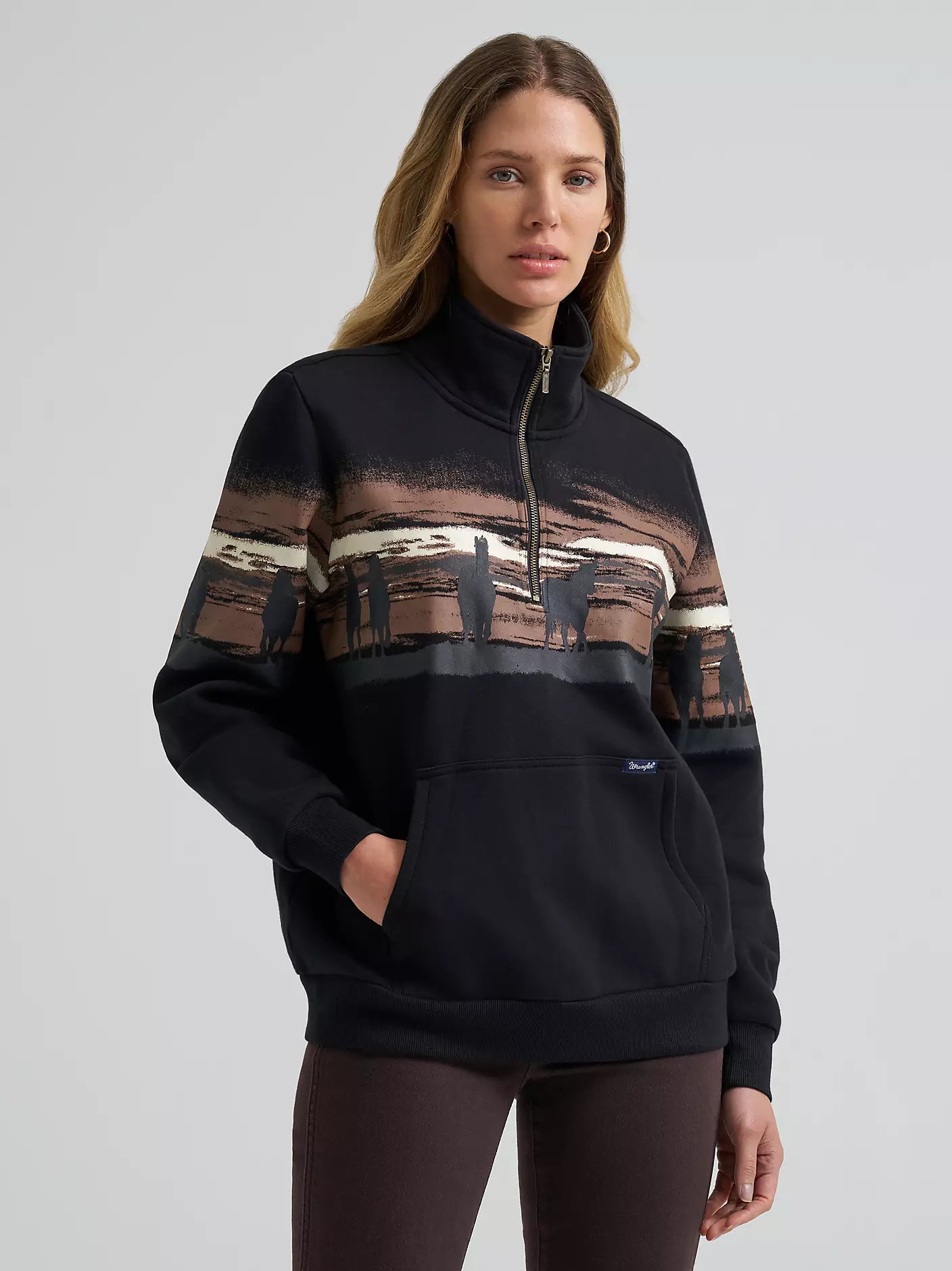 Woman wearing a black Wrangler pullover with patterned sleeves on a gray background