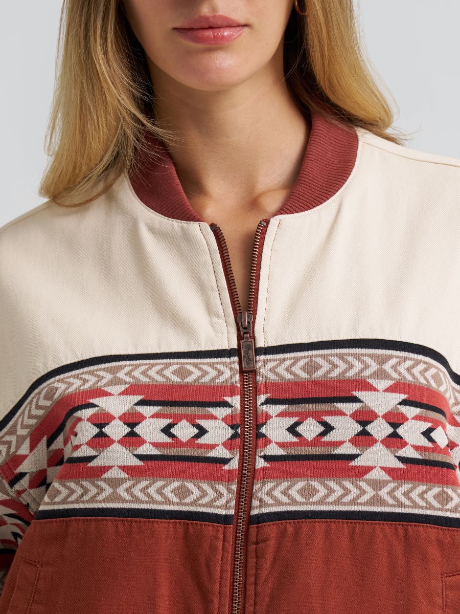 Woman wearing a orange and cream Wrangler bomber jacket, on a grey background
