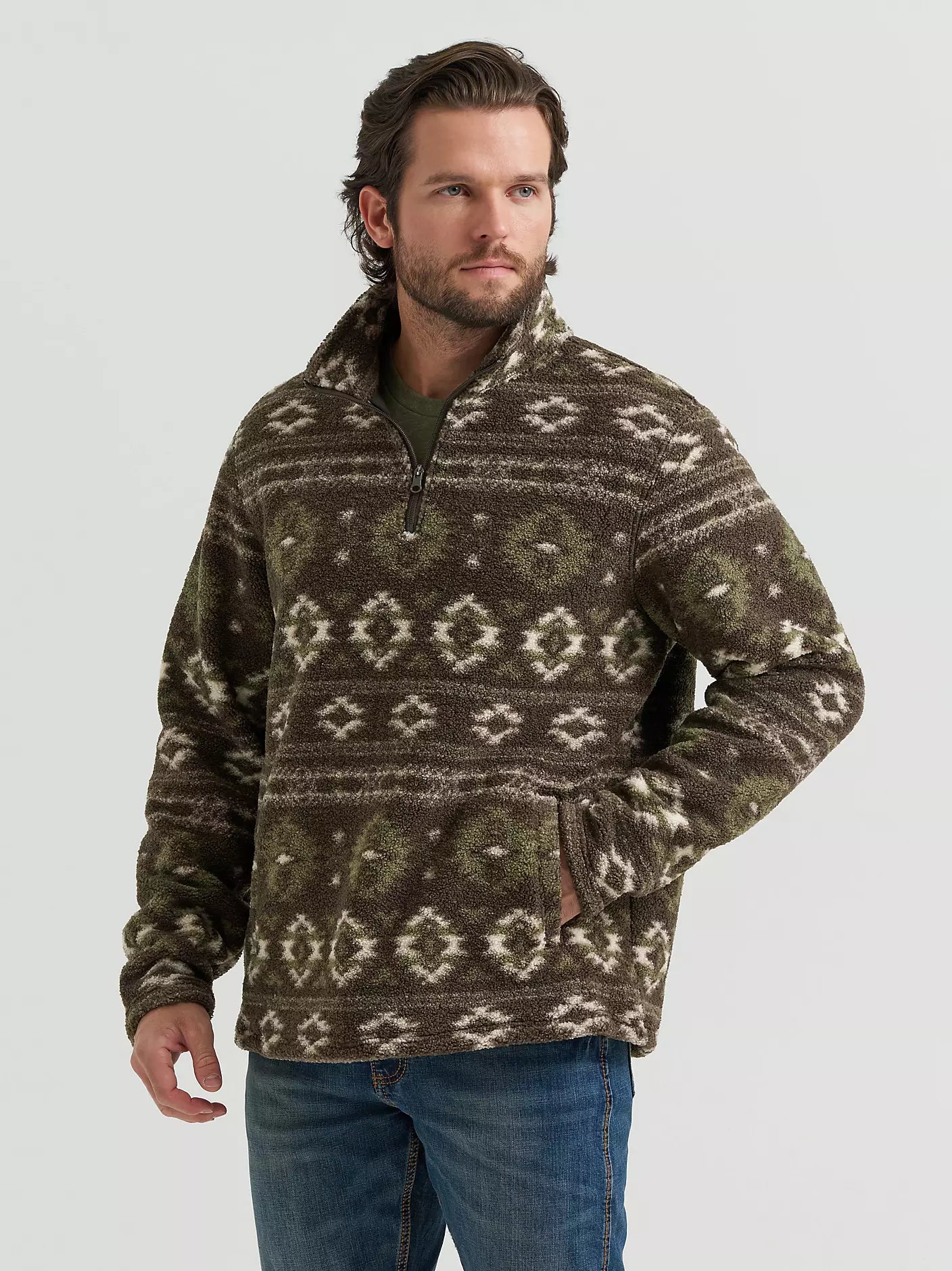 A man wearing a brown and olive green patterned quarter-zip fleece pullover sweater from Wrangler with blue jeans, standing against a light gray studio background.