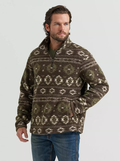 A man wearing a brown and olive green patterned quarter-zip fleece pullover sweater from Wrangler with blue jeans, standing against a light gray studio background.