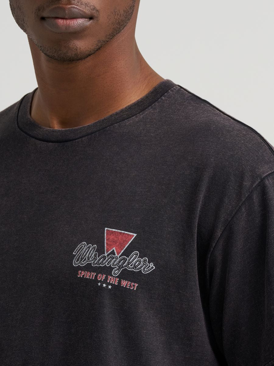 Close up of a man wearing a black Wrangler tshirt with a logo on the chest on a grey background