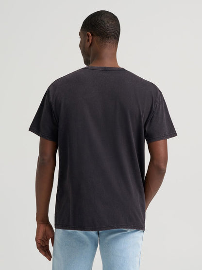 Man wearing a black Wrangler tshirt and blue jeans on a grey background