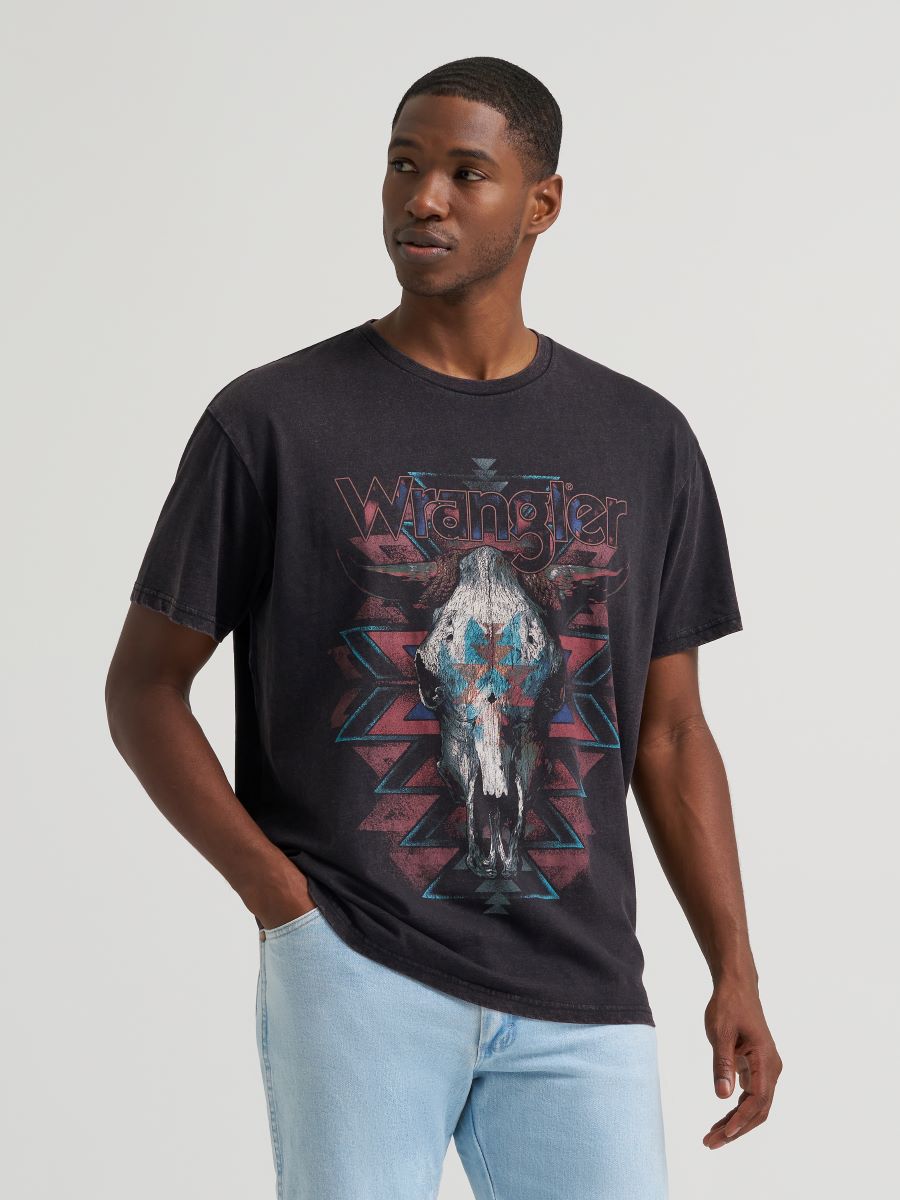 Man wearing a black Wrangler tshirt with a cow skull on it and blue jeans on a grey background