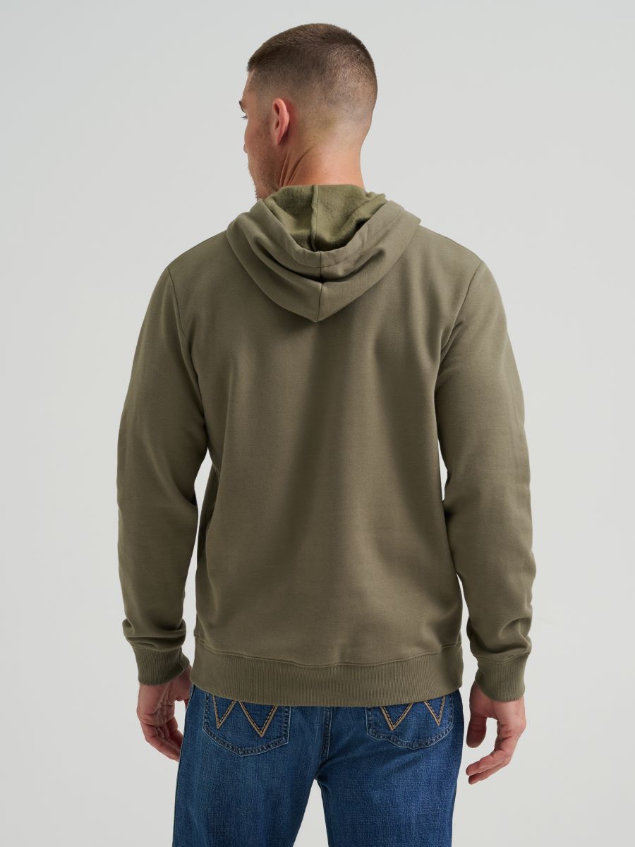 Man wearing a green Wrangler hoodie and blue jeans on a grey background