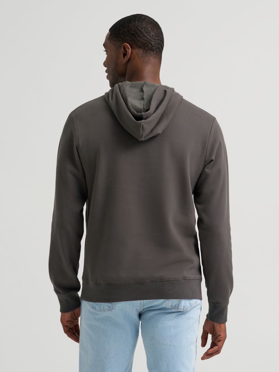 Man wearing a grey Wrangler hoodie and blue jeans on a grey background