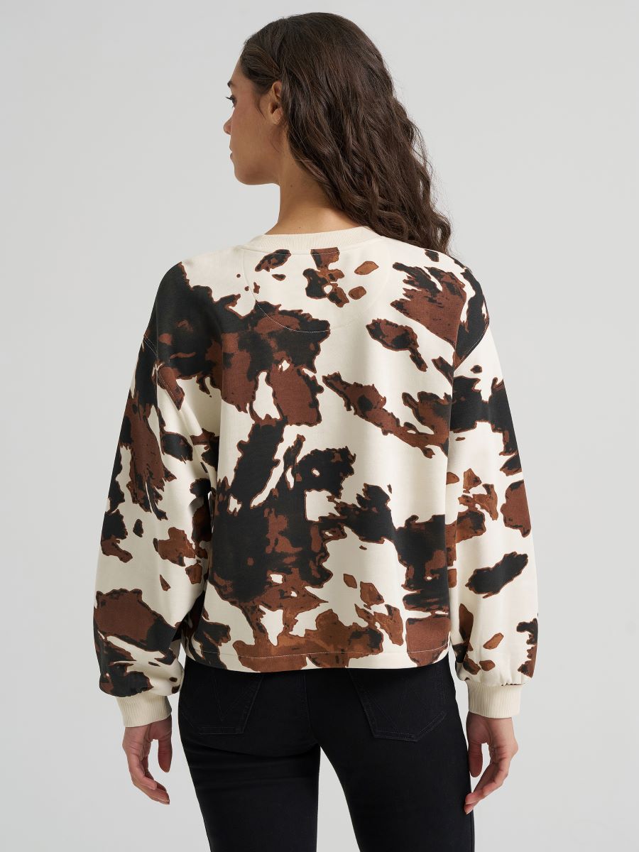 Woman wearing a cow print Wrangler sweater and black jeans on a grey background
