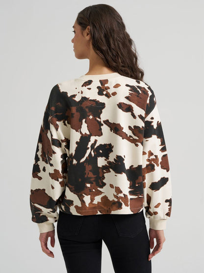Woman wearing a cow print Wrangler sweater and black jeans on a grey background