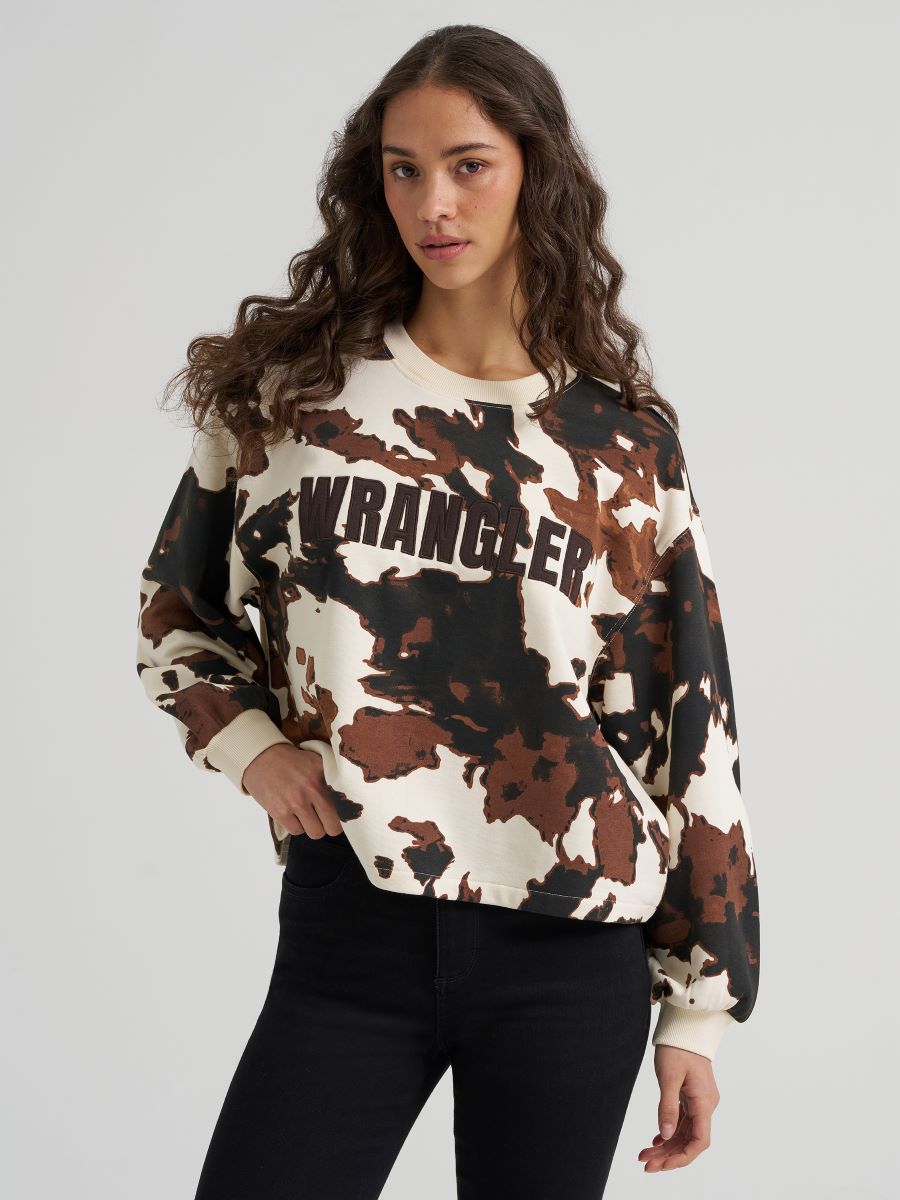 Woman wearing a cow print Wrangler sweater and black jeans on a grey background