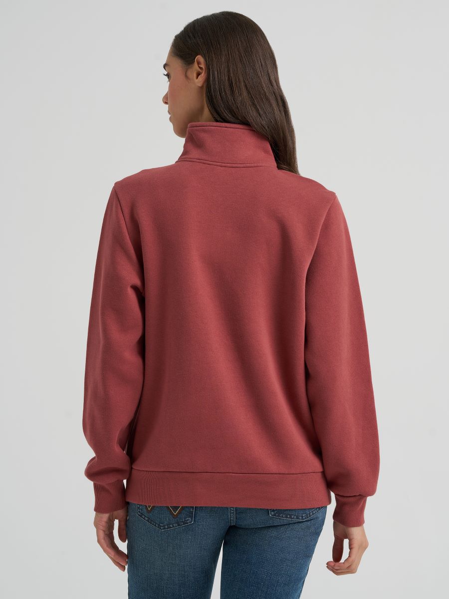 woman wearing a rose colored Wrangler sweater and blue jeans on a grey background