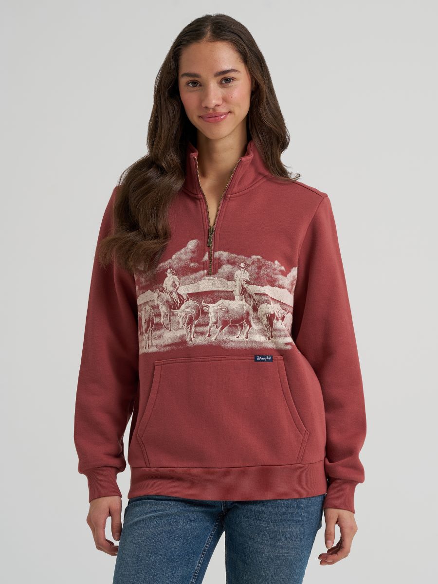 woman wearing a rose colored Wrangler sweater and blue jeans on a grey background