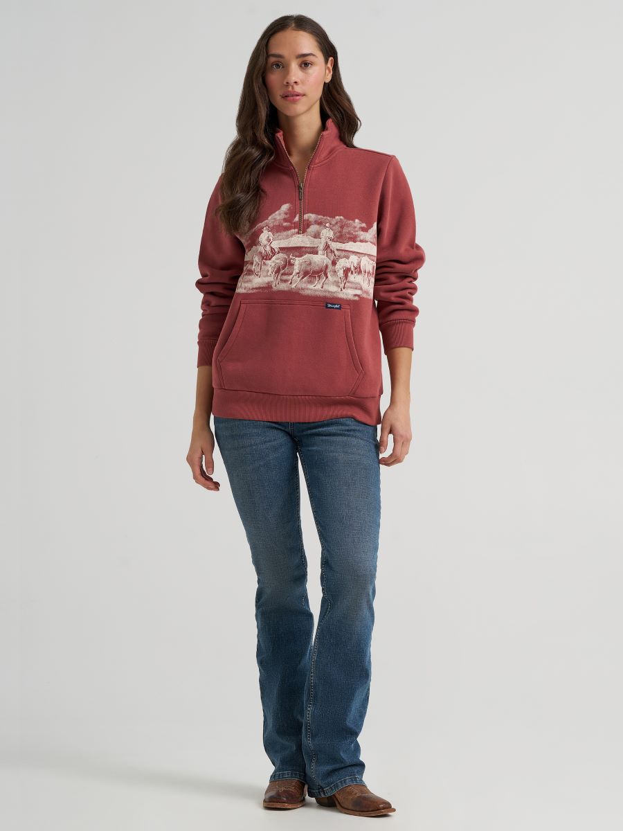 woman wearing a rose colored Wrangler sweater and blue jeans on a grey background
