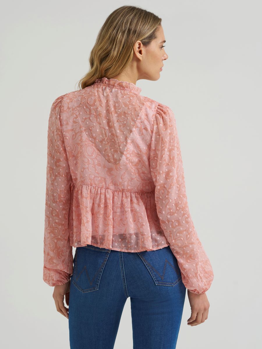 Woman wearing a sheer pink Wrangler blouse and blue jeans on a grey background