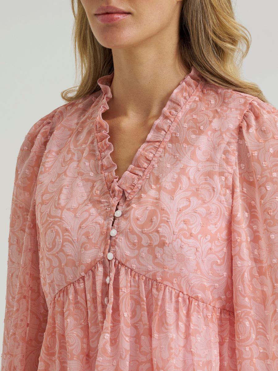 Woman wearing a sheer pink Wrangler blouse on a grey background