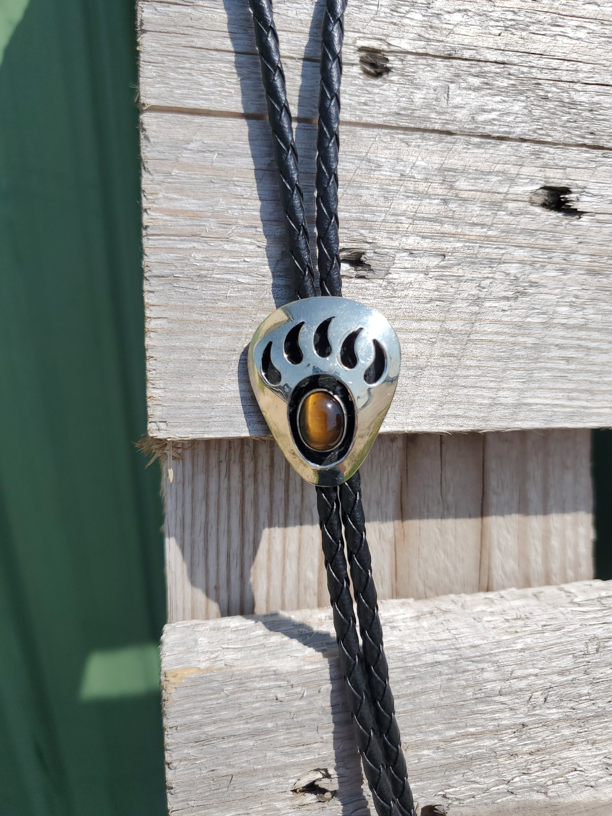 a bear claw pendant bolo tie with a brown stone in an outdoor setting