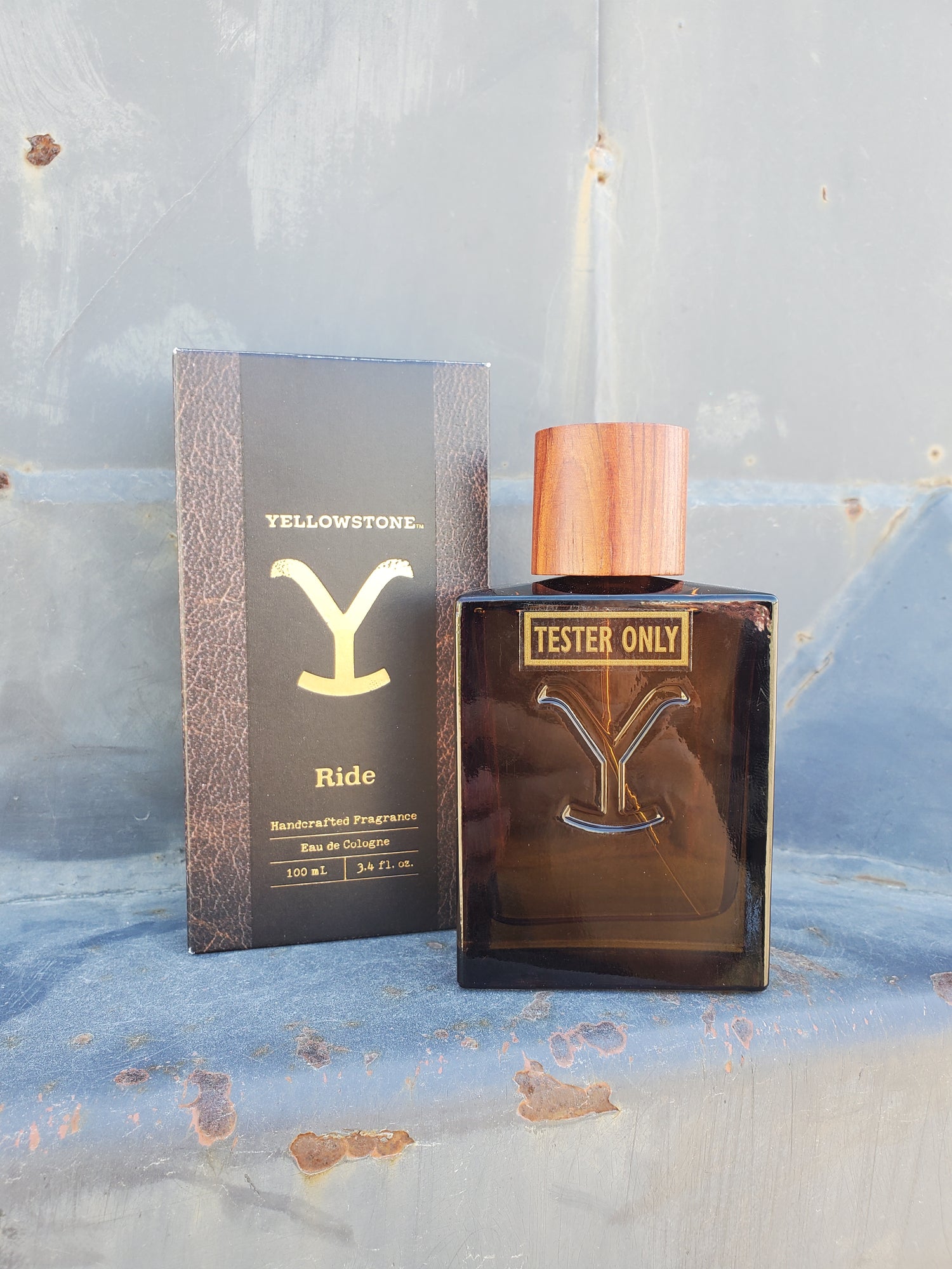A men's cologne bottle with a wooden cap and a label that reads 'Yellowstone Ride' and 'Tester Only'. The bottle is in front of a box with a similar label.