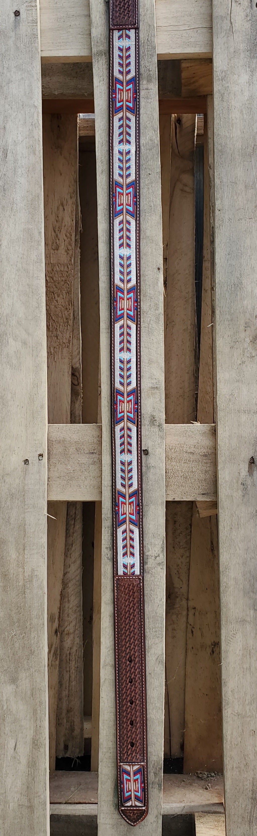 Lengthwise view of a leather belt with a 'fletching' design on a wooden background