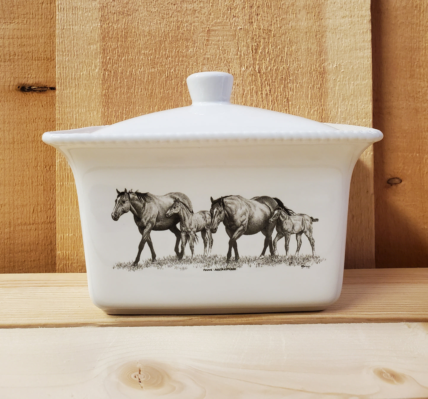 A white ceramic butter dish with a lid, featuring a black and white illustration of two mares and two foals
