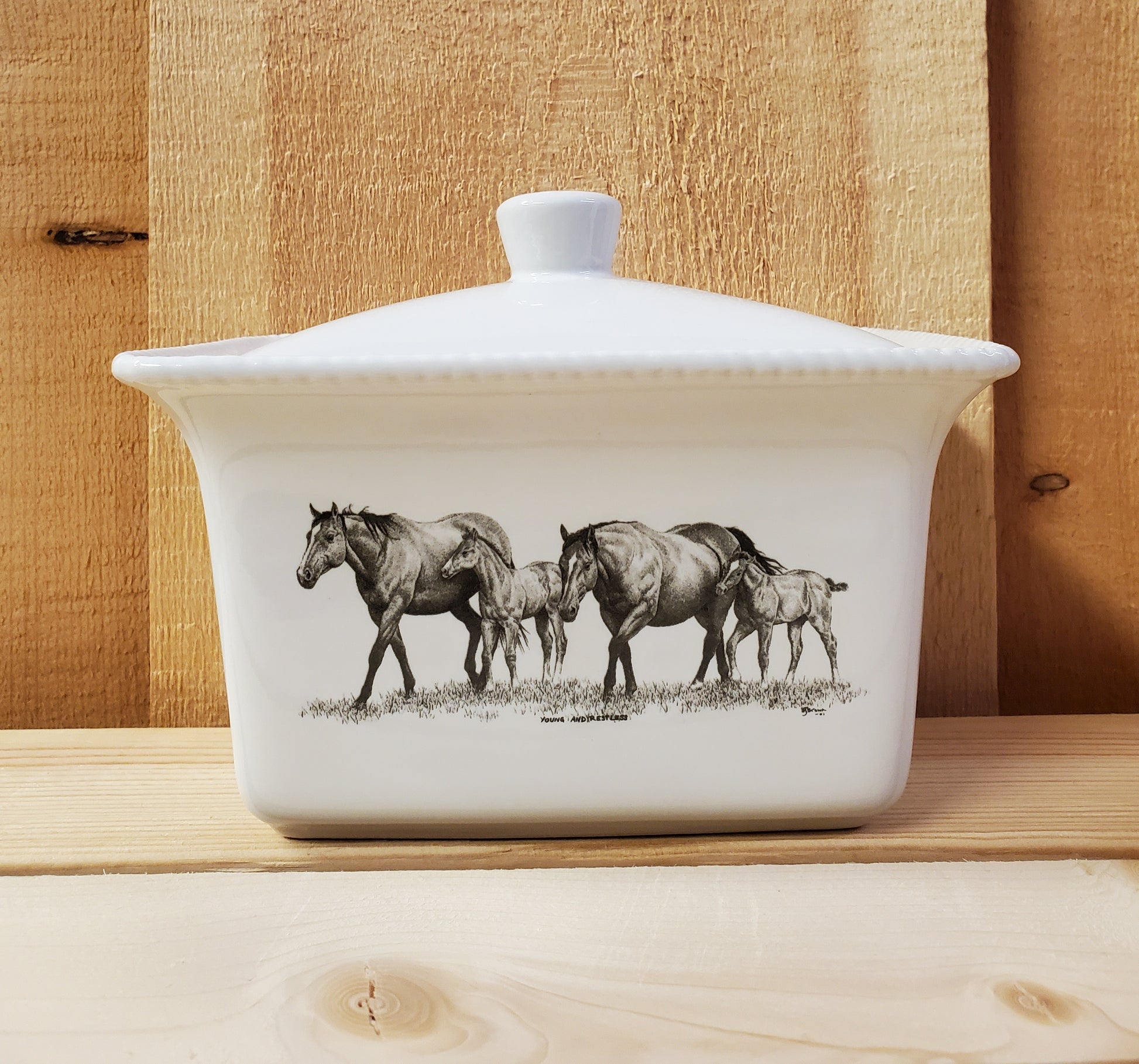 A white ceramic butter dish with a lid, featuring a black and white illustration of two mares and two foals