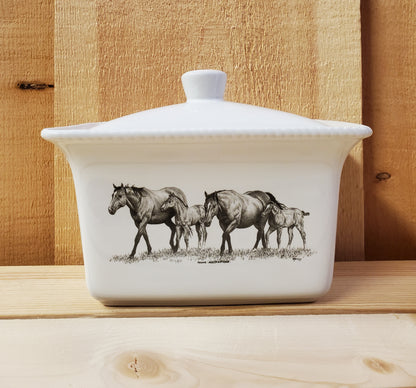 A white ceramic butter dish with a lid, featuring a black and white illustration of two mares and two foals