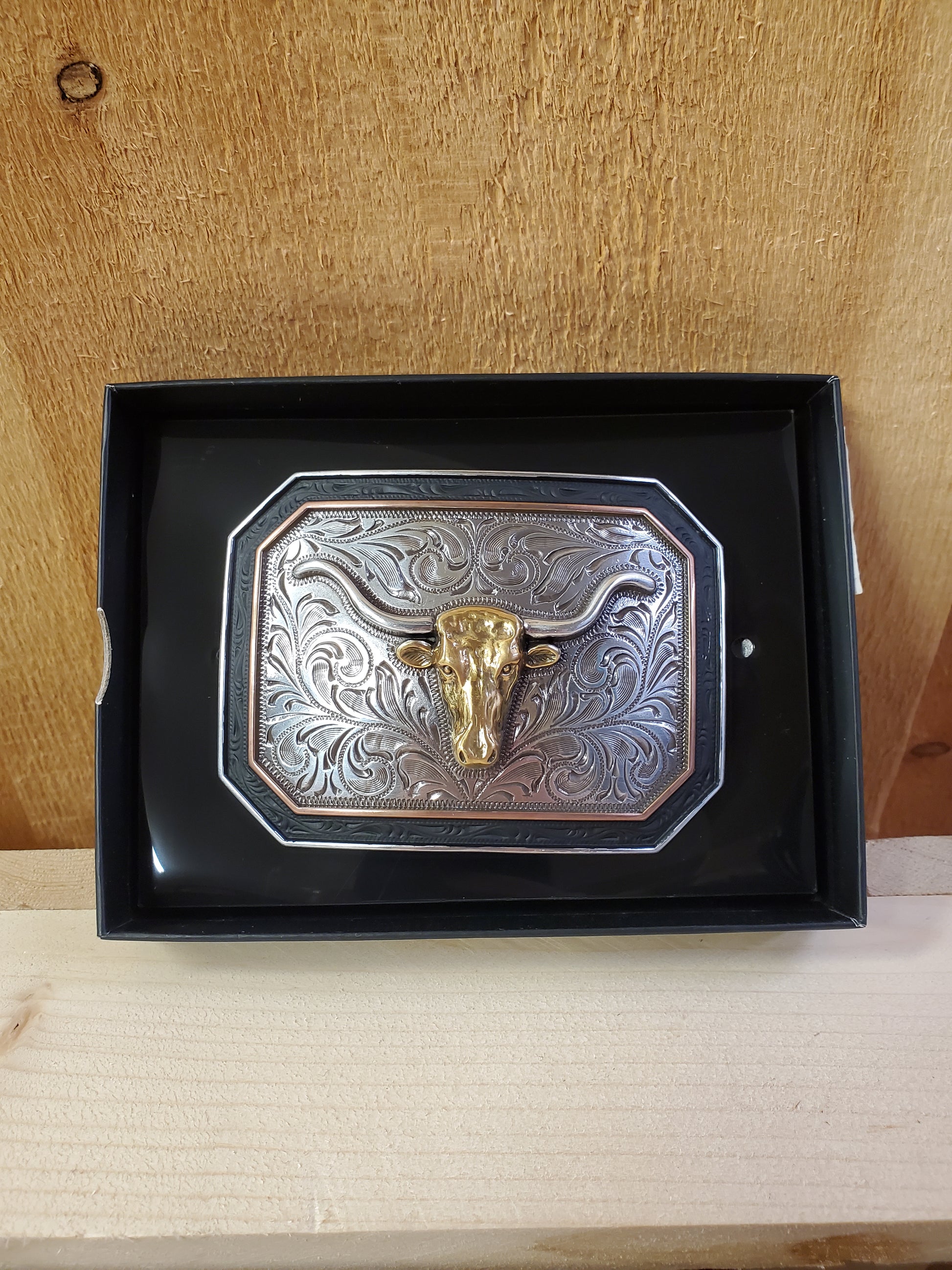 Steerhead belt buckle with black and copper trim in a black box on a wooden background