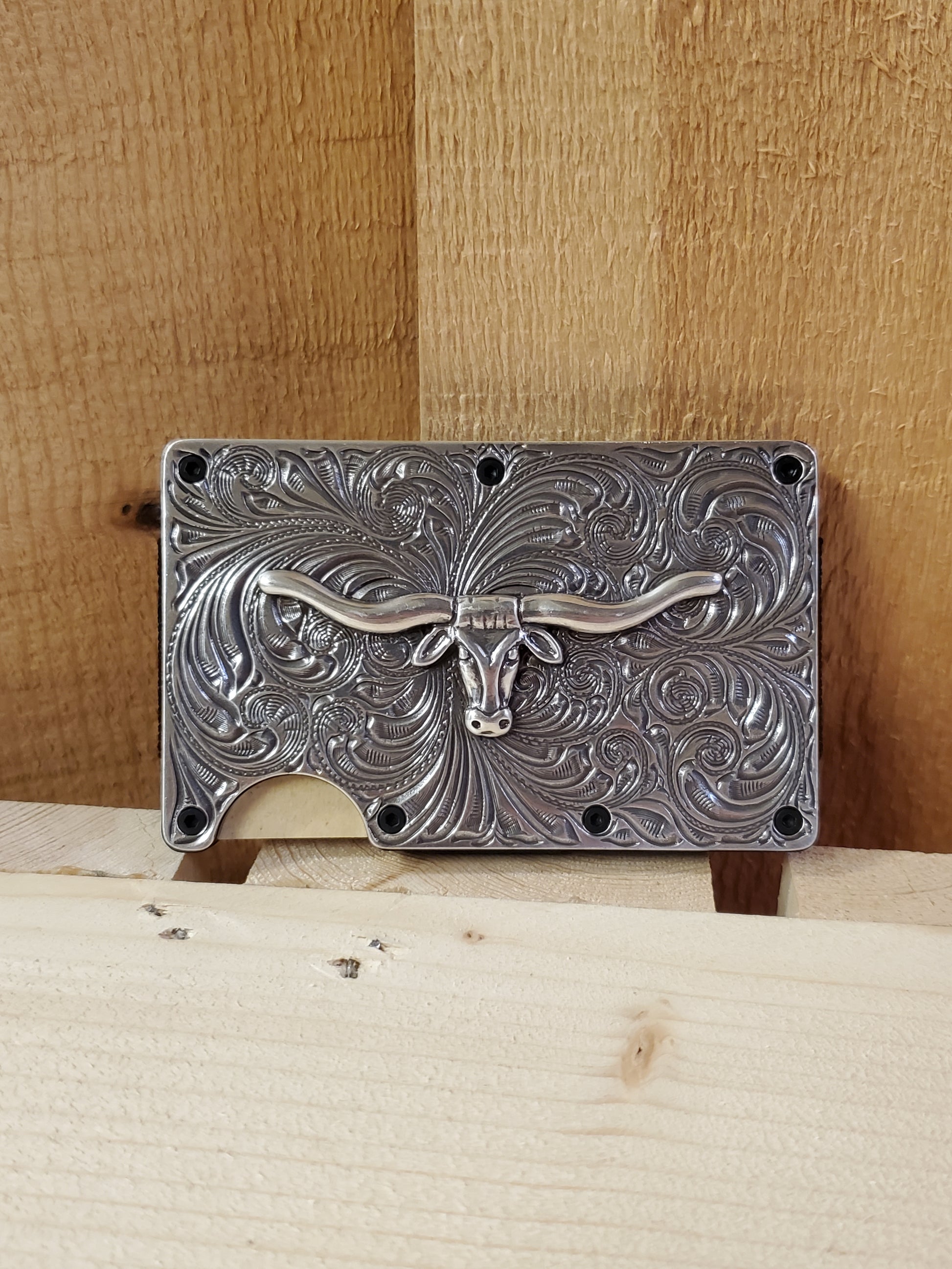 Antique finish longhorn utility wallet with decorative engraving, displayed against a wooden background.