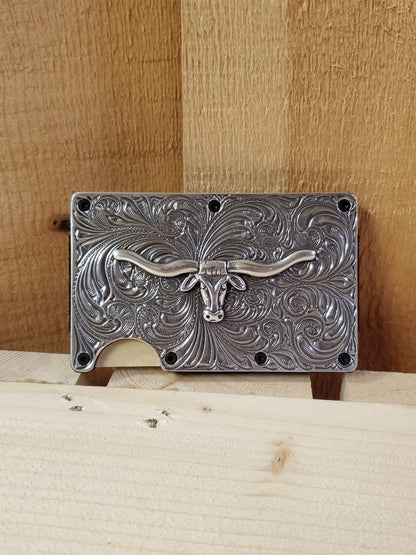 Antique finish longhorn utility wallet with decorative engraving, displayed against a wooden background.